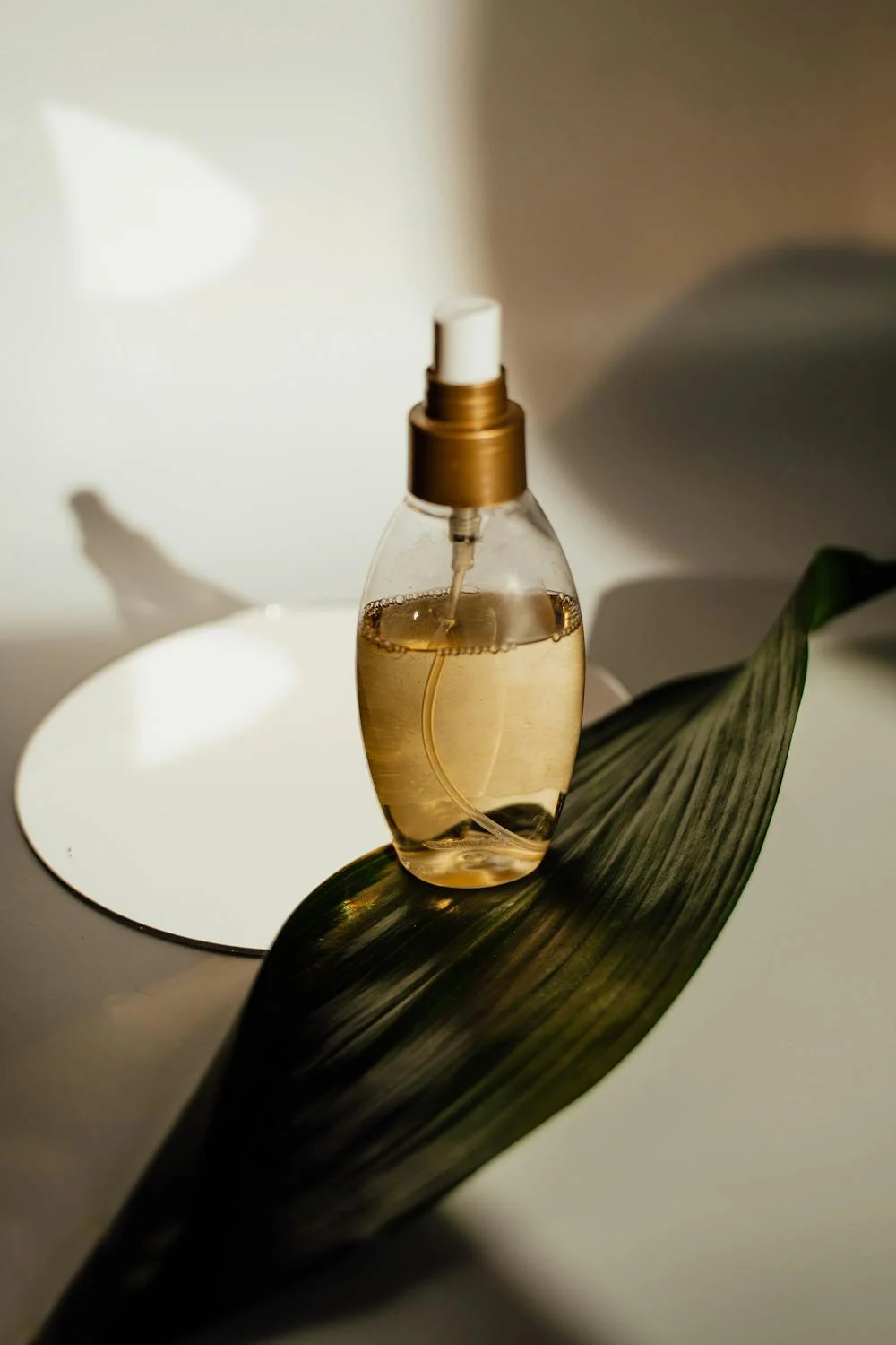 Transparent spray bottle with golden liquid on a green leaf, blurred background. Showcases the impact of background removal for creating professional, eye-catching product images on e-commerce platforms like Etsy